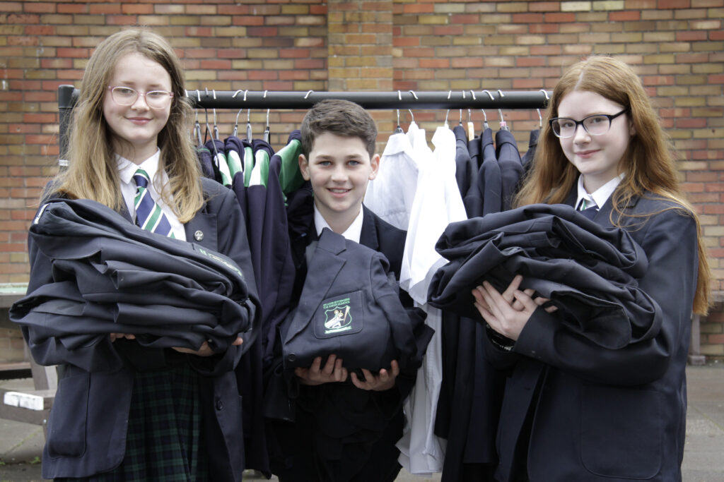 Three school children holding school uniforms