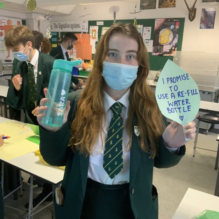 Girl at Down High School holding a green water bottle in her left hand and a paper leaf with 'I promise to use a re-fill water bottle' in her right hand.