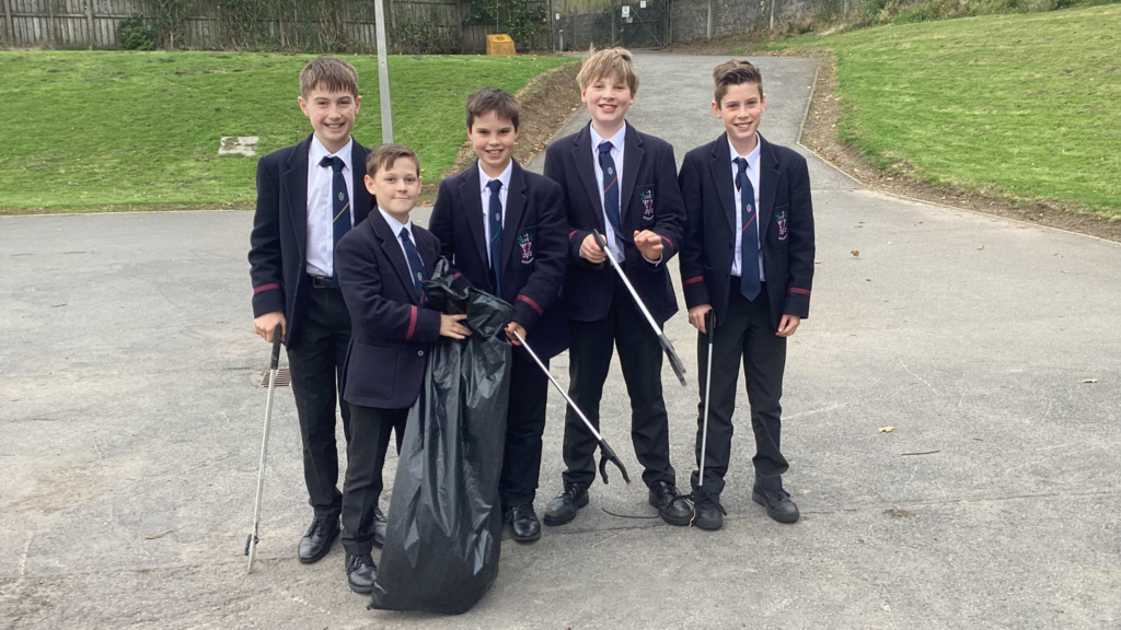 Group of five boys in school unifrom outside carrying litter picking gear and a black bin bag