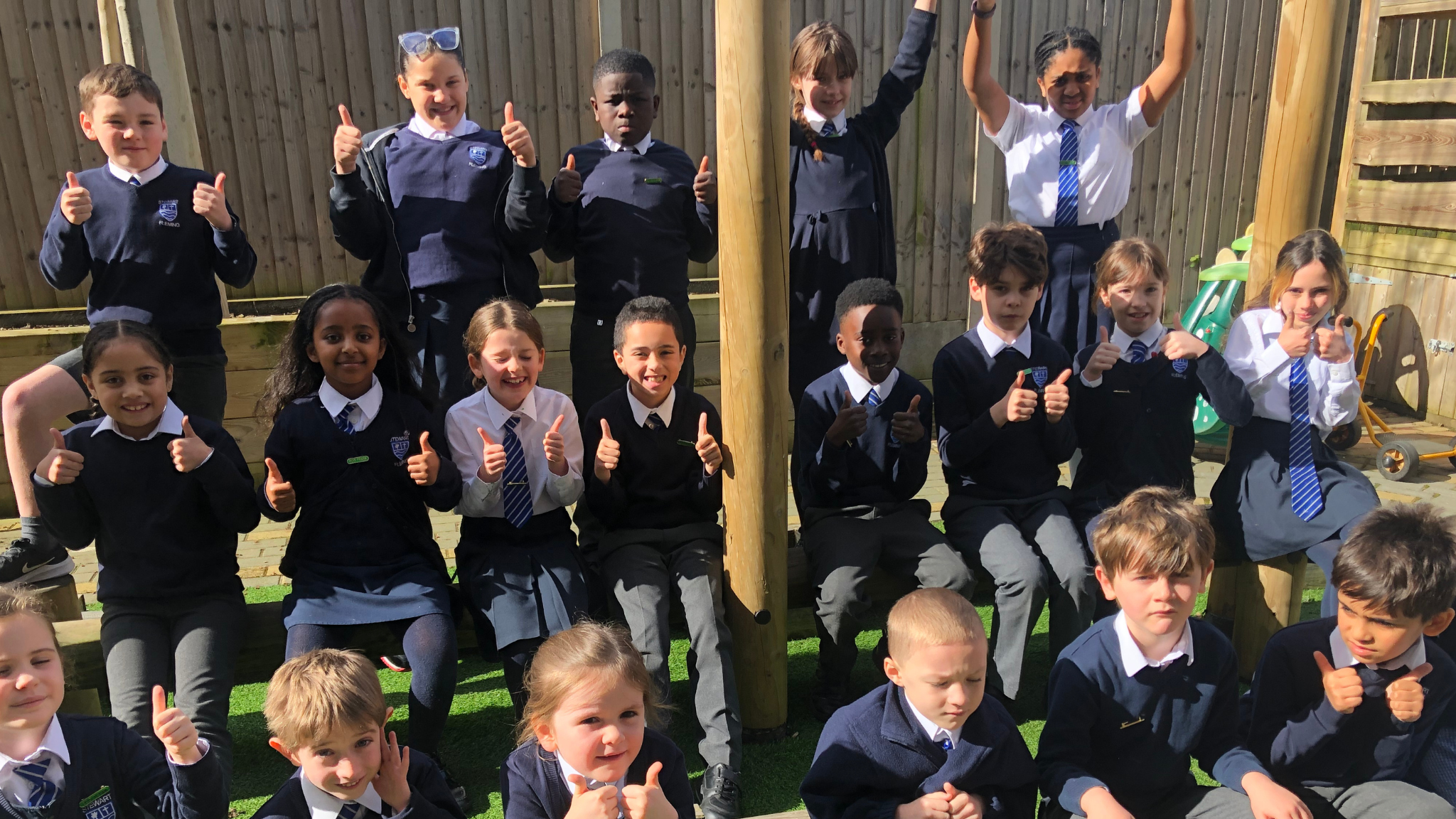 Group of children outside sitting in their playground with their thumbs up