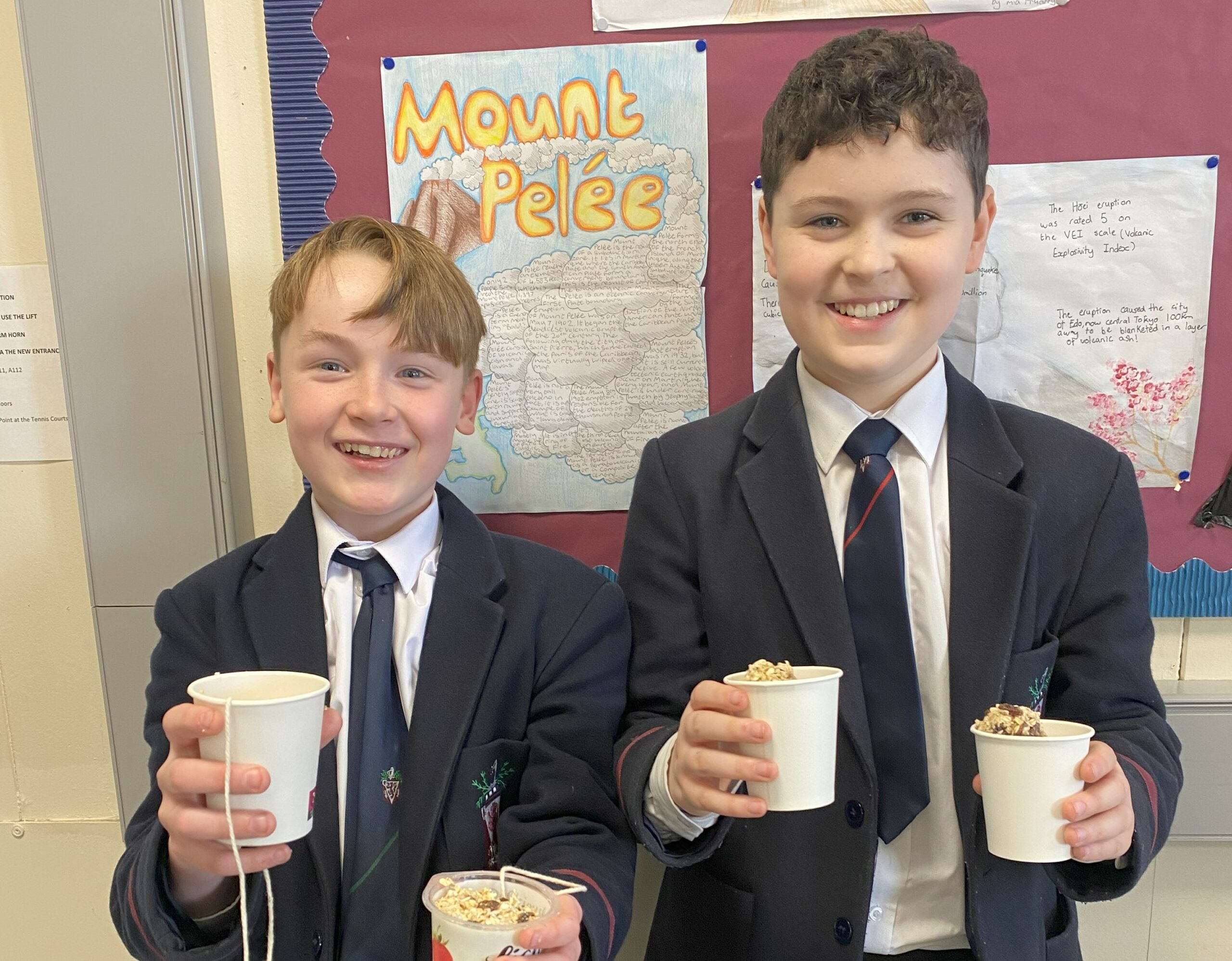 Two boys in school uniform smiling at the camera holding bird feed in cups