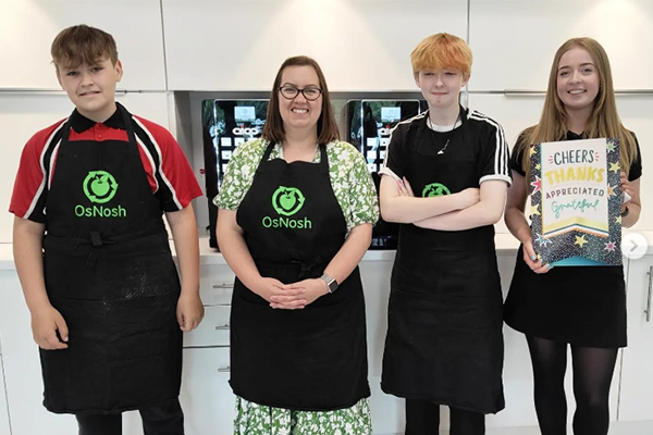 Three students and a teacher are stood together wearing OsNosh aprons.