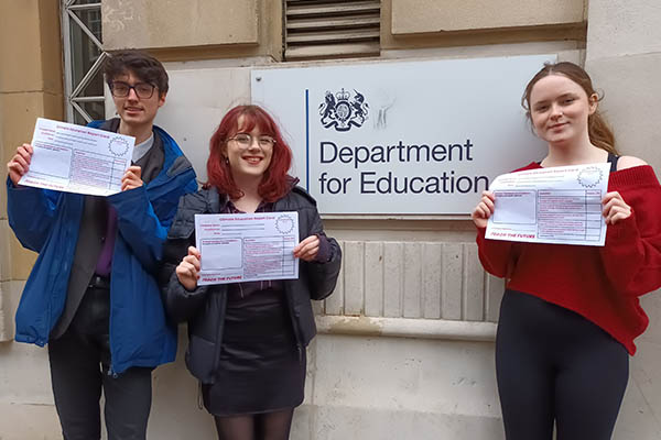 Three students are stood outside the Department of Education to hand in a petition.